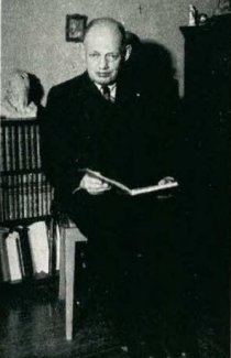 Rudolf Spielmann posa con un libro en sus manos, detrs de l hay una pequea librera repleta de libros